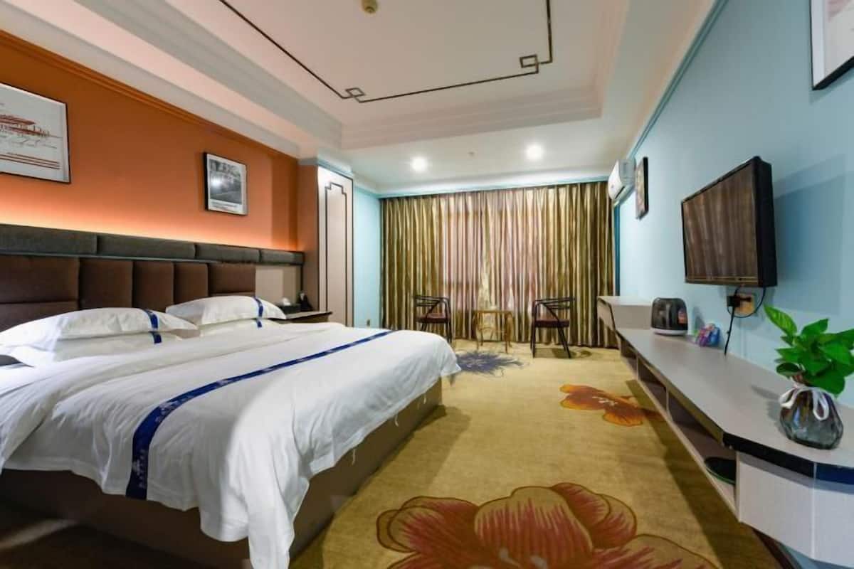 A hotel room with a bed, a desk, a chair, a television, and a plant.