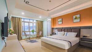 A hotel room with a large bed, a desk, a chair, a TV, and a window with curtains. - Zhuxin Business Hotel (Huidong)