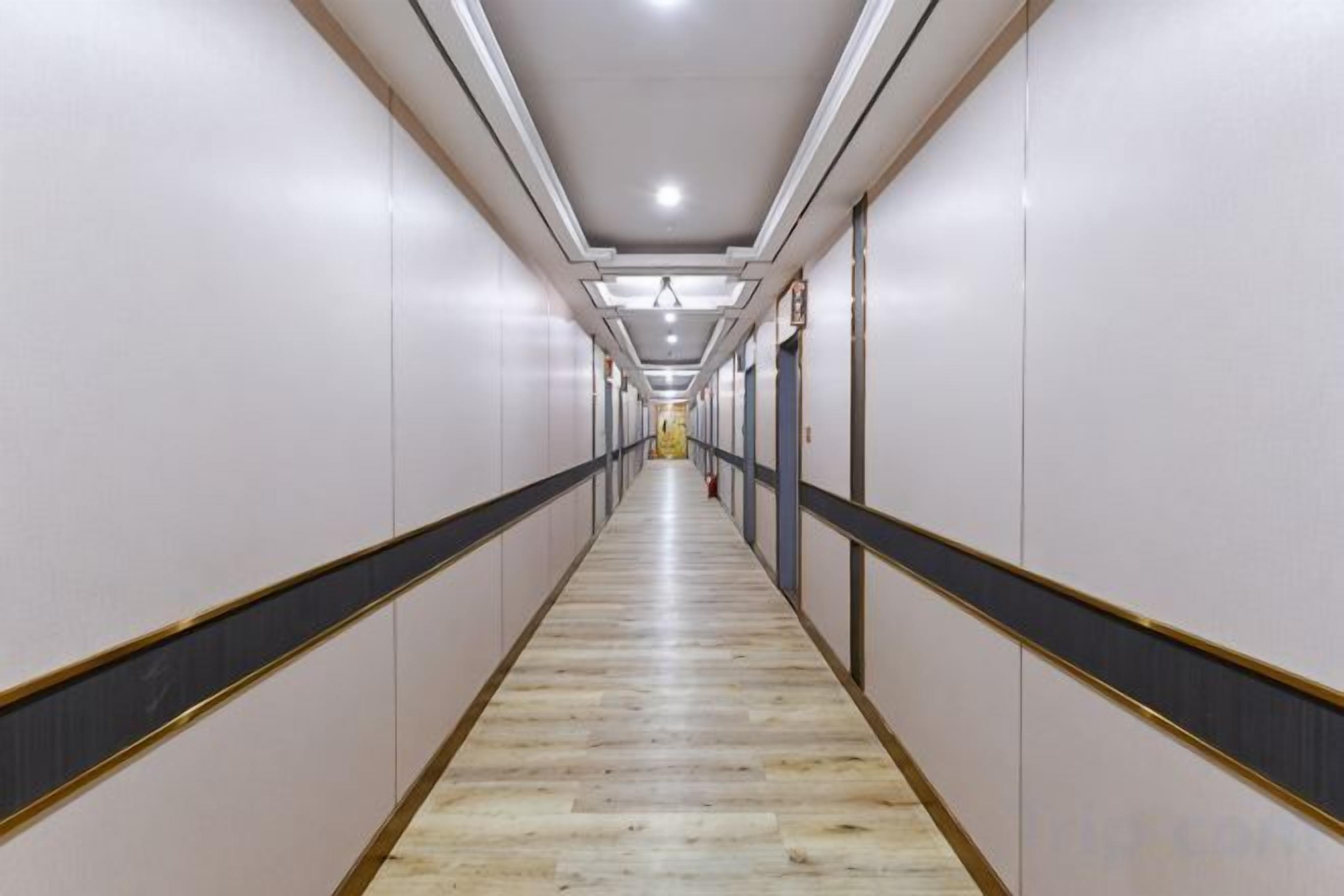 A long, narrow hallway with a wooden floor and white walls, leading to a distant door.