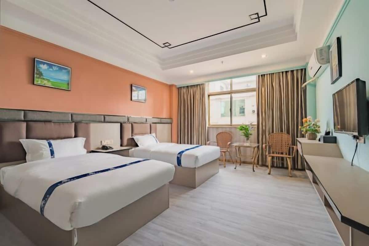 A hotel room with two beds, a desk, a chair, a TV, and a window with curtains.