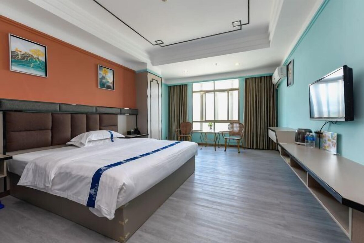 A hotel room with a large bed, a desk, a chair, and a television.