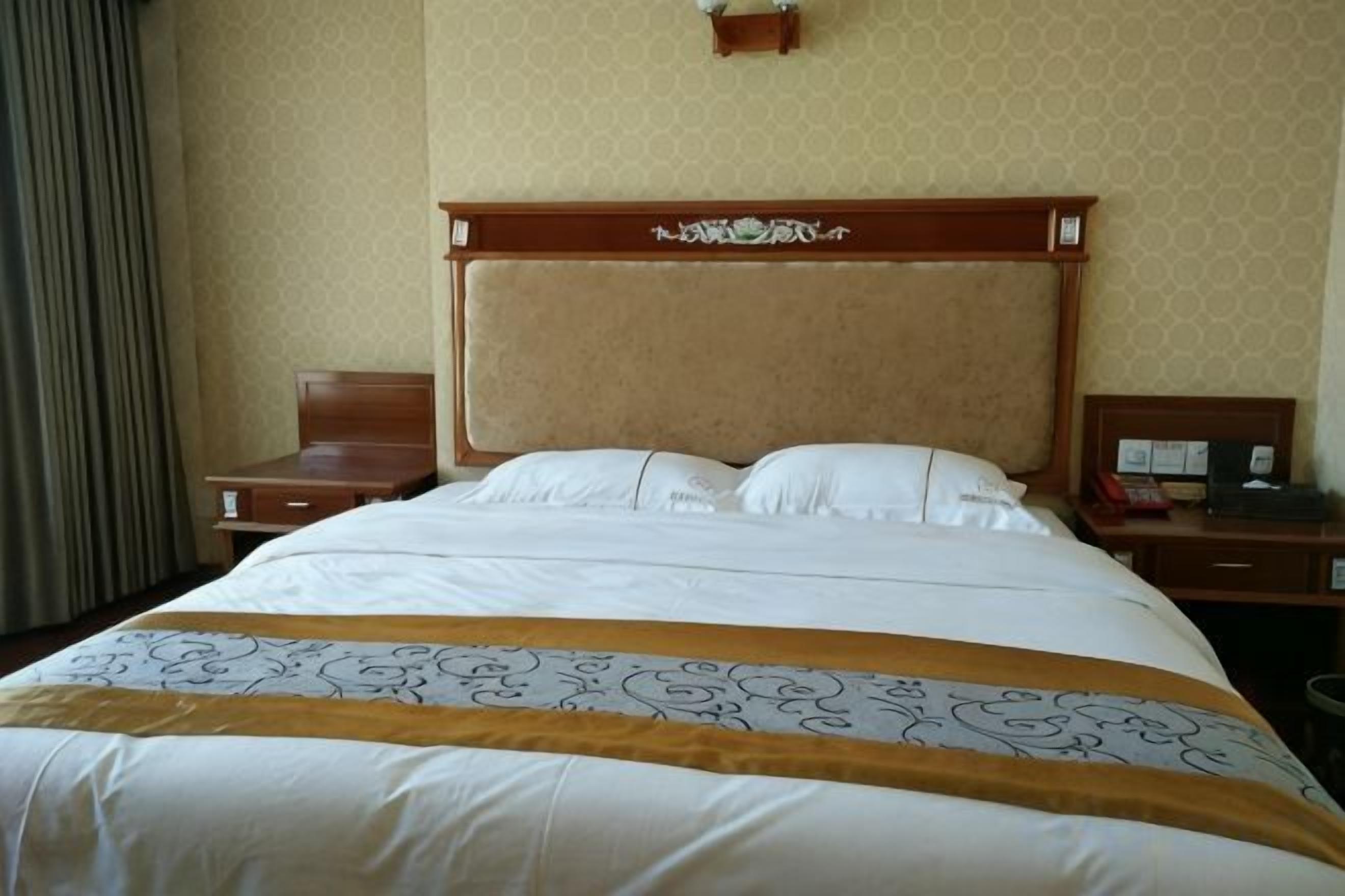 A hotel room with a large bed, a wooden headboard, a bedside table, and a nightstand.
