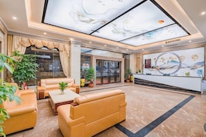 Een hotel lobby met leren banken, een receptiebalie en een muurschildering aan het plafond.