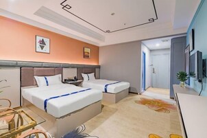 Quarto de hotel com duas camas, uma mesa de trabalho, televisão e banheiro visível por uma porta aberta.