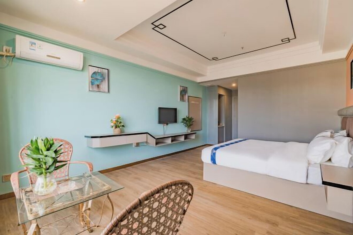 A modern hotel room with a bed, a TV, a small table with a plant, and a chair.