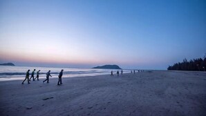 A beach with people walking, a clear sky, and distant landforms. - Zhuxin Business Hotel (Huidong)