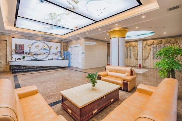 A hotel lobby with a reception desk, seating area, and a large digital display. - Zhuxin Business Hotel (Huidong)