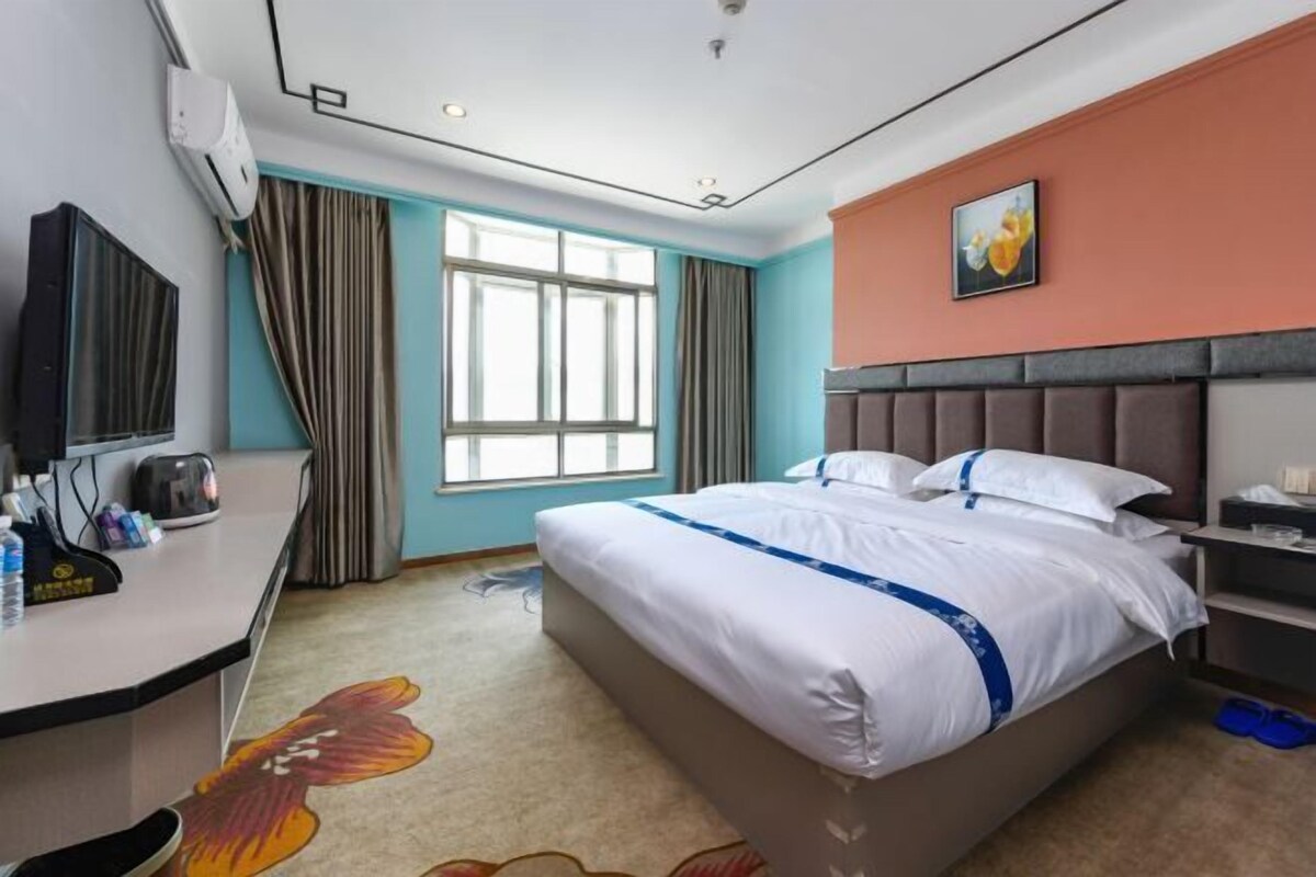 A hotel room with a bed, a desk, a television, and a window with curtains.