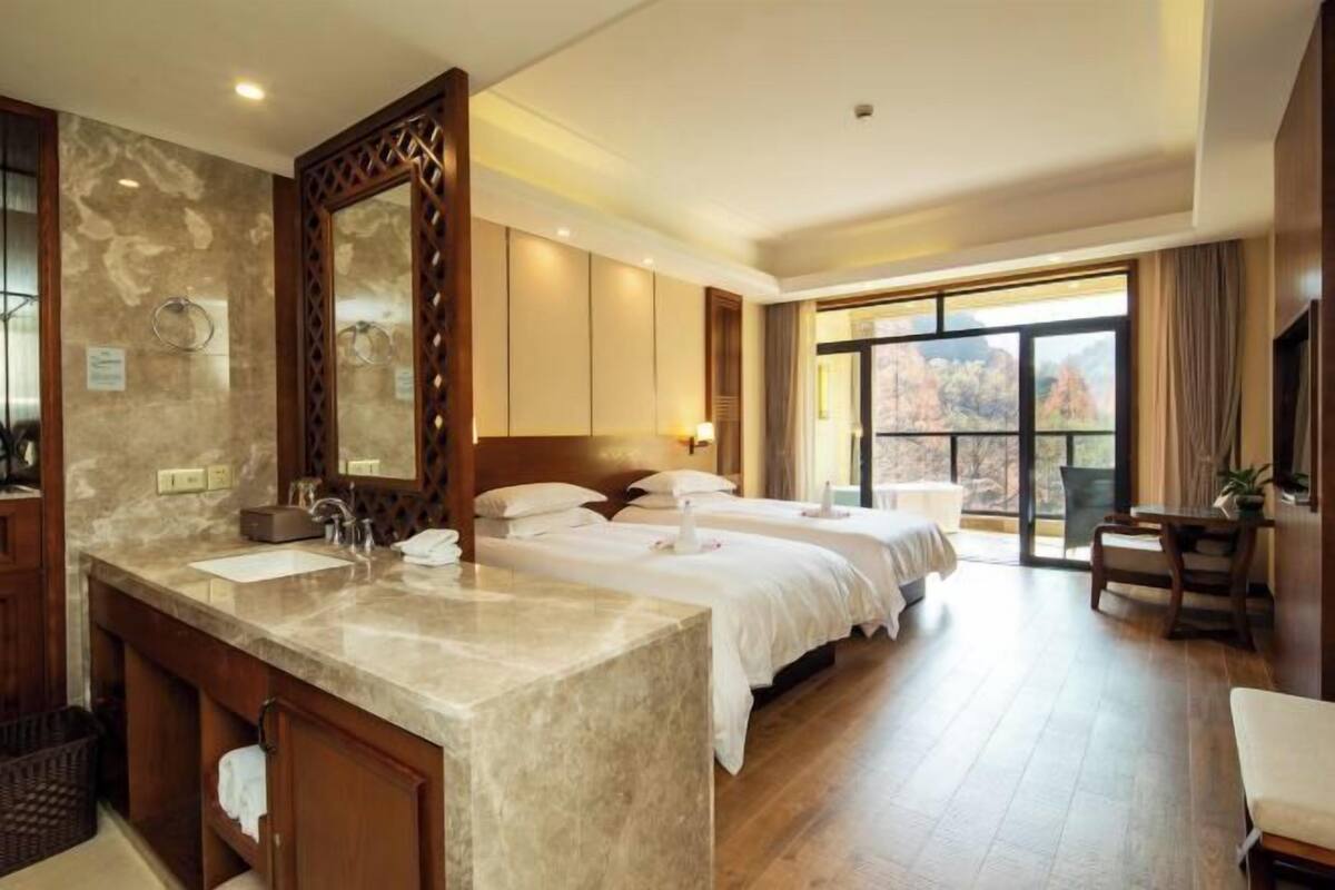 A hotel room with a large bed, a separate bathroom with a marble vanity, and a large window offering a view.