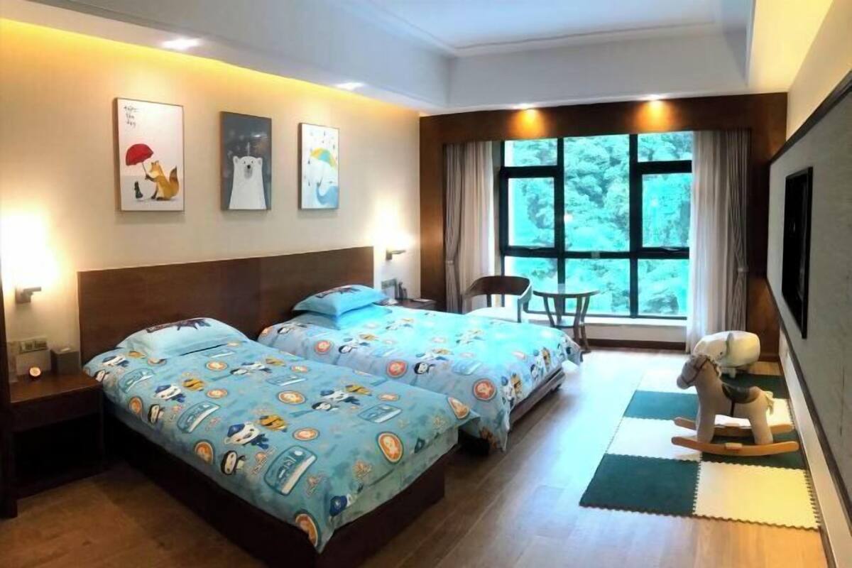A hotel room with two beds, a rocking horse, a window with a view, and artwork on the wall.