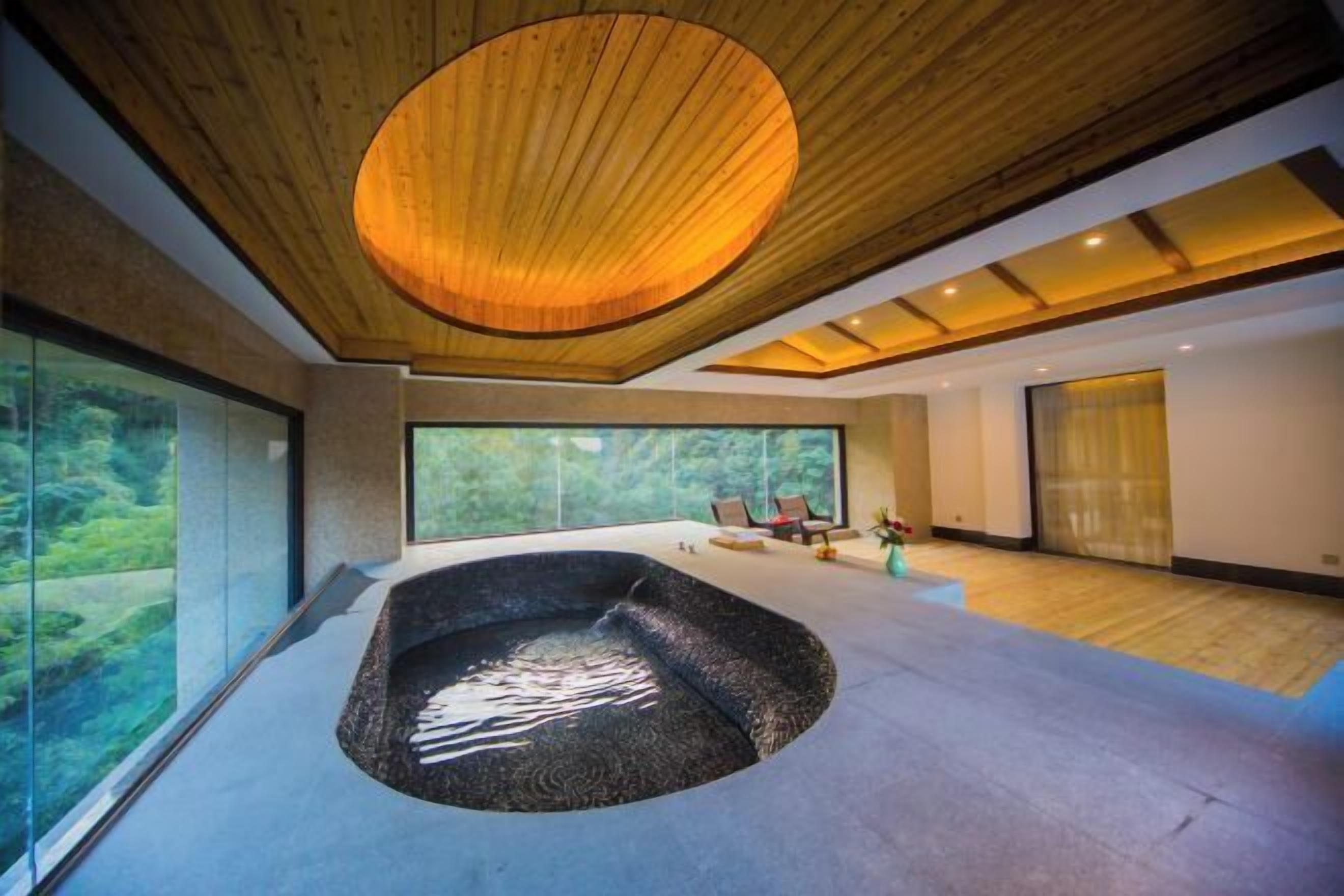 Een moderne spa ruimte met een groot bubbelbad, houten plafond en grote ramen met uitzicht op de omgeving.