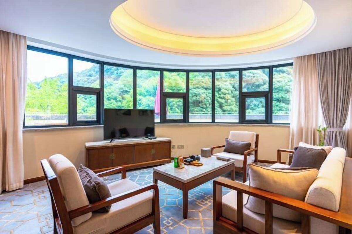 A hotel room with a large window, a flat-screen TV, a wooden coffee table, and a sofa.