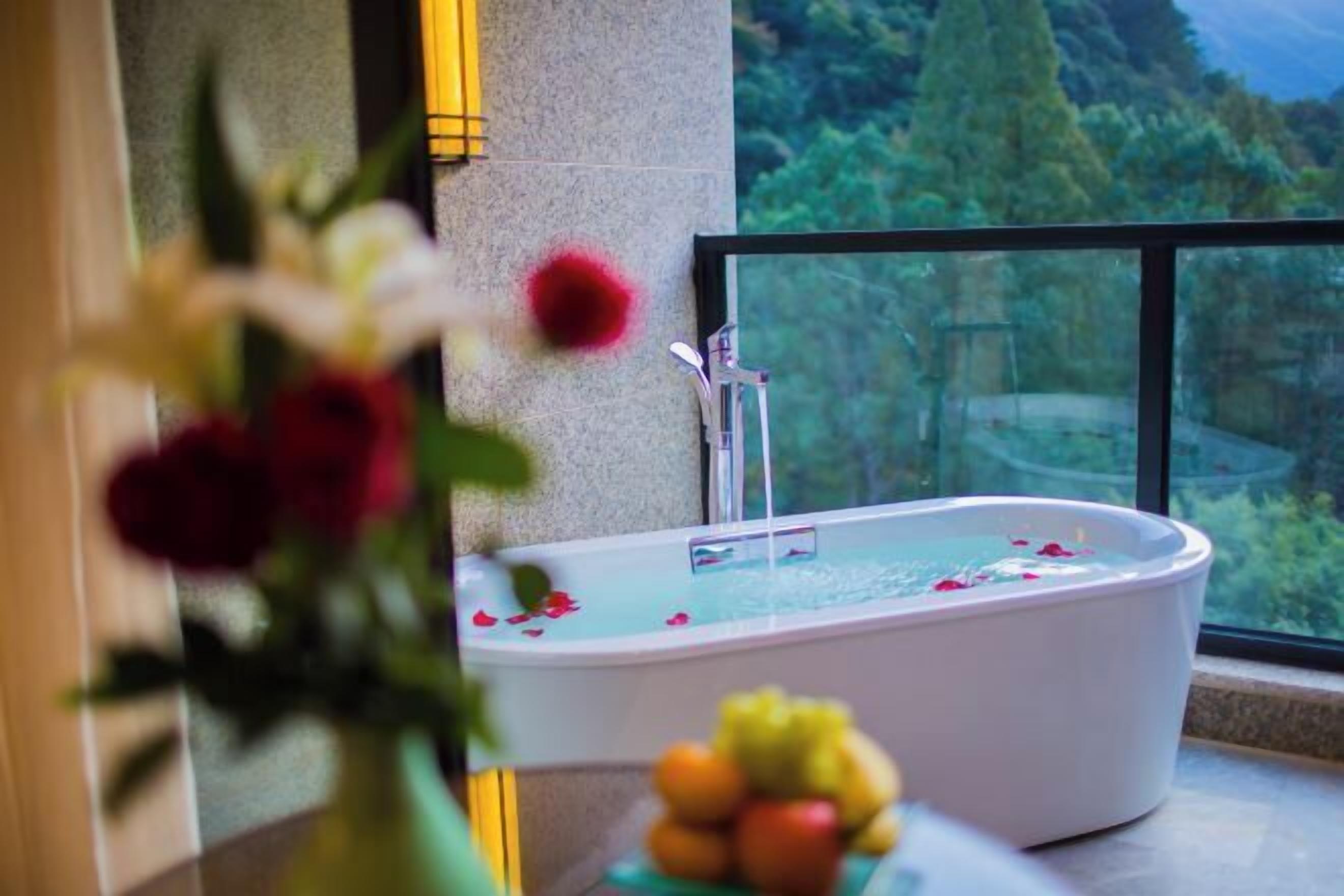 A bathtub with rose petals, a fruit bowl, and a vase of flowers.