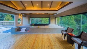 A modern interior with a wooden deck, a seating area with wicker furniture, and a large window offering a view of a forest. - Tianmingshan Spa & Resort (Ninghai)
