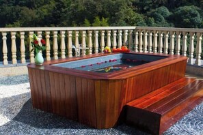 A wooden hot tub with a built-in bench, surrounded by a stone patio, and a balustrade railing. - Tianmingshan Spa & Resort (Ninghai)