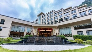 A modern hotel with a prominent entrance, a landscaped garden, and a clear sky. - Tianmingshan Spa & Resort (Ninghai)