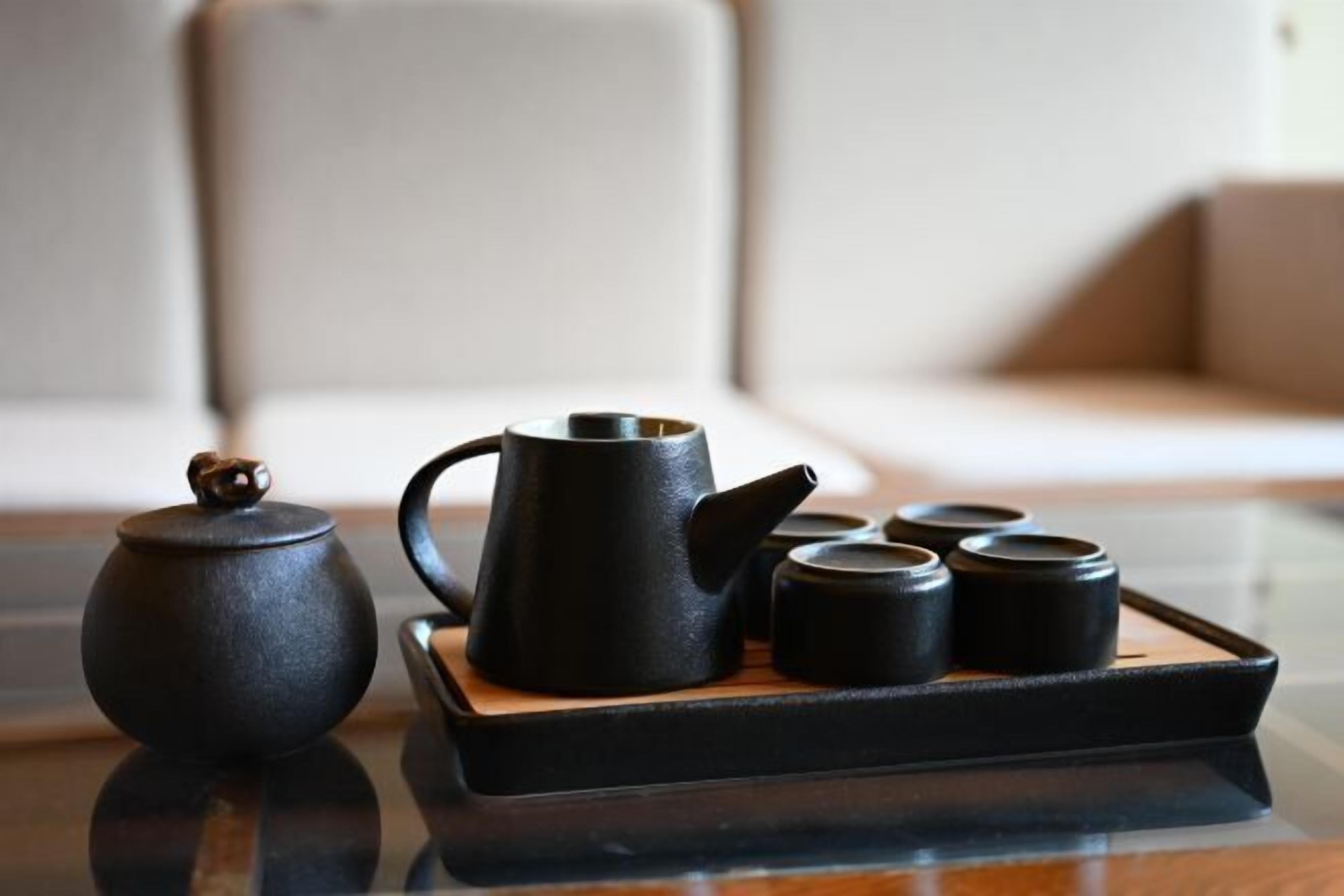 A black teapot and four black cups on a tray.