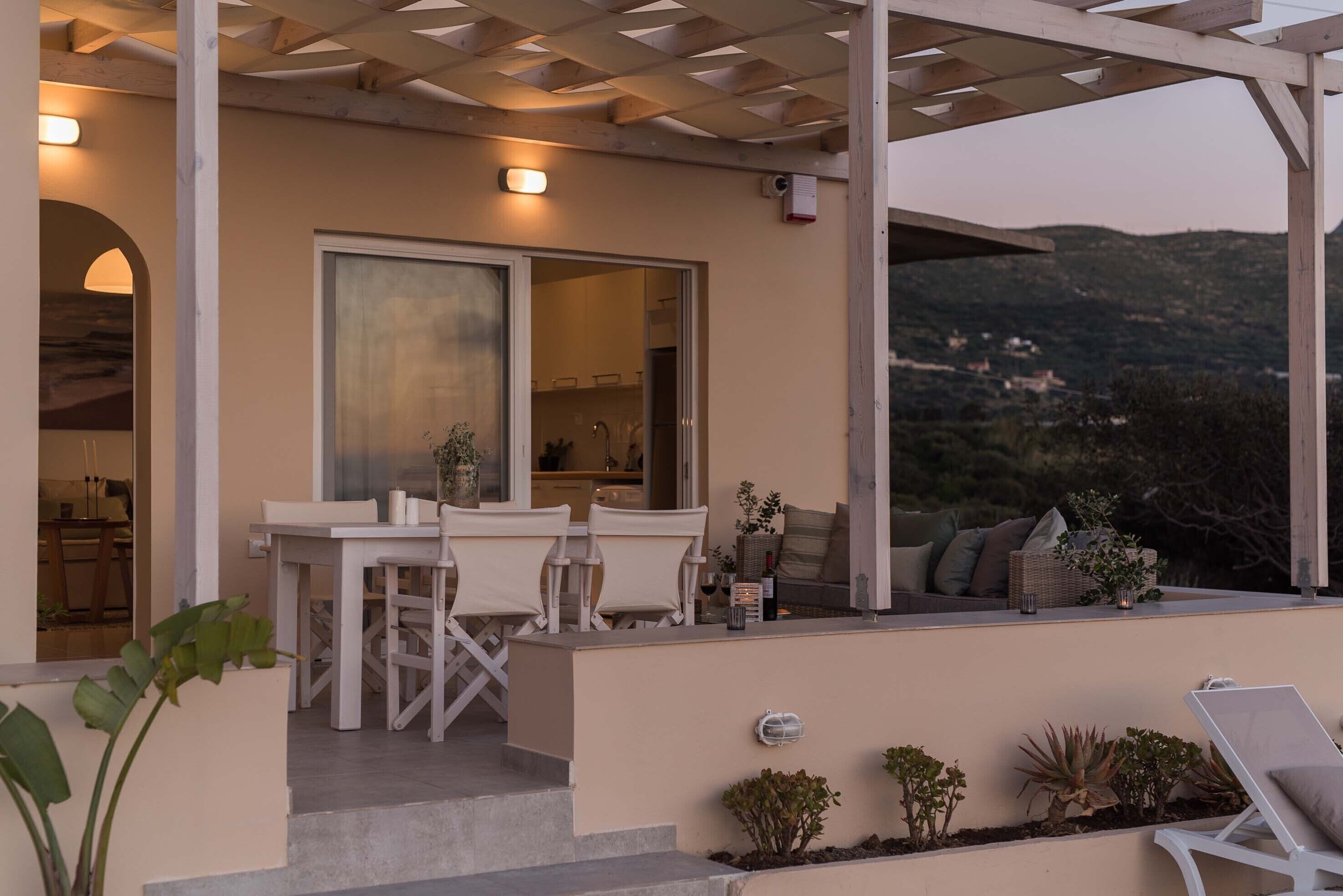 Ein überdachter Sitzbereich im Freien mit Tisch und Stühlen, Blick ins Innere sowie ein Balkon mit Pflanzen und Kissen.