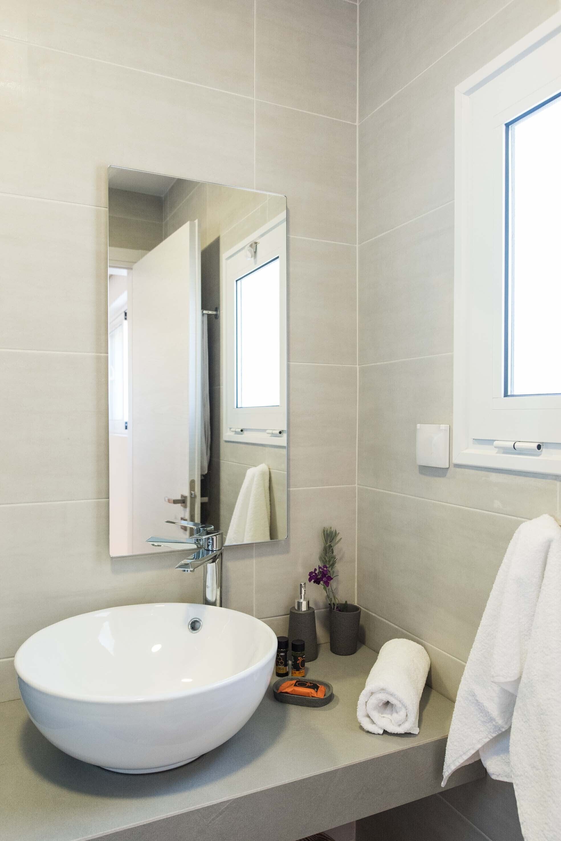 A modern bathroom with a large white sink, a mirror, and a window.