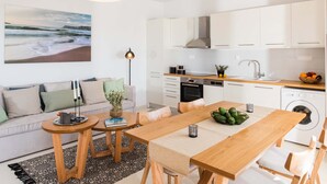 A modern kitchen with white cabinets, a central island, and a dining area with a wooden table and chairs. - Falasarna Seafront House (Kissamos)