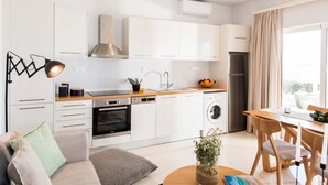 A modern kitchen with white cabinets, a built-in oven, a washing machine, and a dining area with a wooden table and chairs. - Falasarna Seafront House (Kissamos)