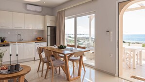 A modern kitchen with white cabinets, a dining area with wooden chairs, and a large window overlooking the sea. - Falasarna Seafront House (Kissamos)