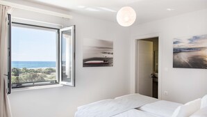 A bedroom with a large window, a bed, and artwork on the walls. - Falasarna Seafront House (Kissamos)