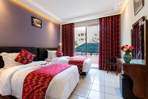 Ein Hotelzimmer mit zwei Betten, roter und weißer Bettwäsche, einem Schreibtisch mit einer Vase und Blick auf ein Gebäude.
