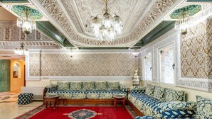 Una habitación lujosa con techo y paredes ornamentadas, un amplio sofá y un tapete rojo estampado.