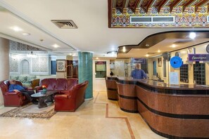 Un hall d’entrée avec des canapés en cuir, un comptoir d’accueil et un plafond orné de motifs.