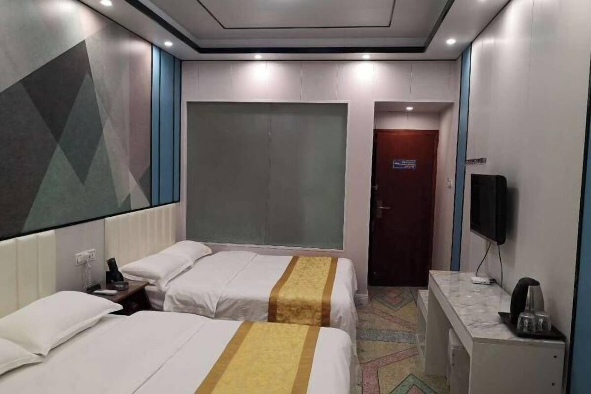 A hotel room with two beds, a TV, a desk, and a door leading to another room.