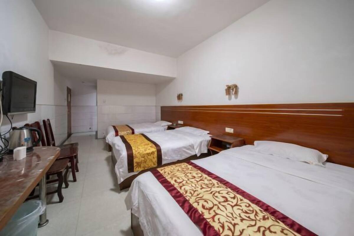 A hotel room with three beds, a wooden headboard, a television, and a dining area with chairs and a table.