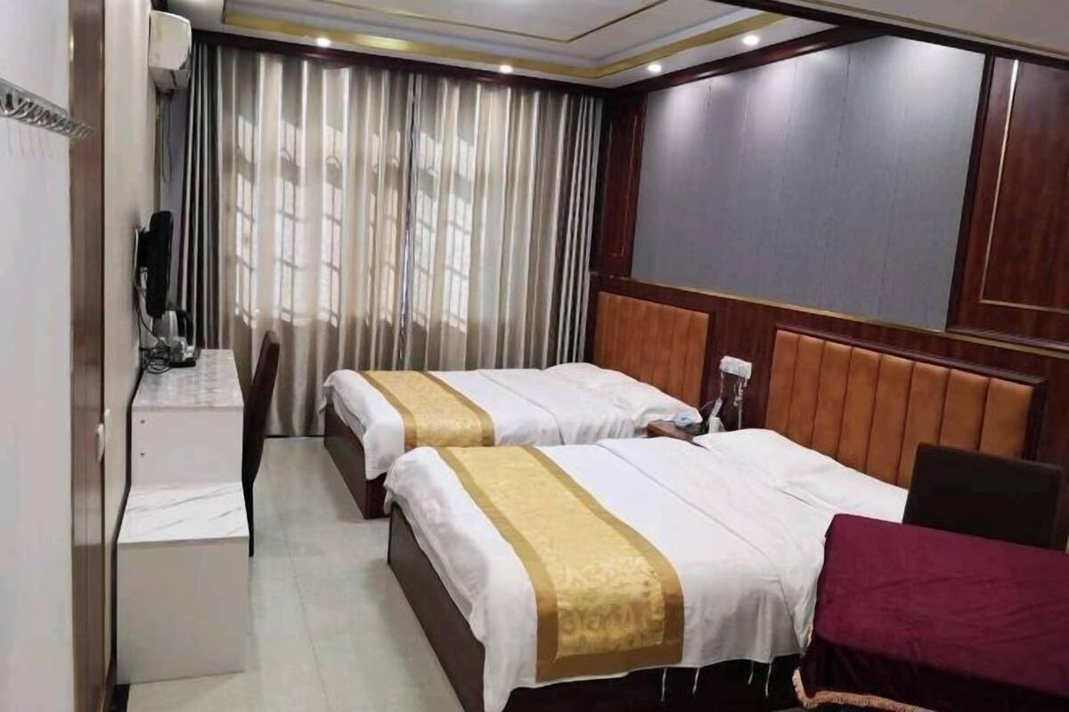 A hotel room with two beds, a desk, a chair, and a TV.