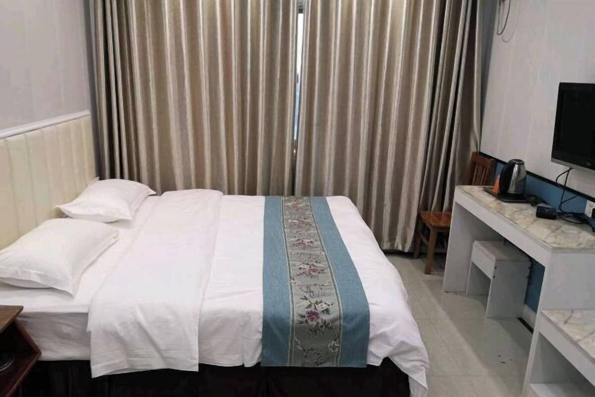 A hotel room with a bed, curtains, a desk, and a television.