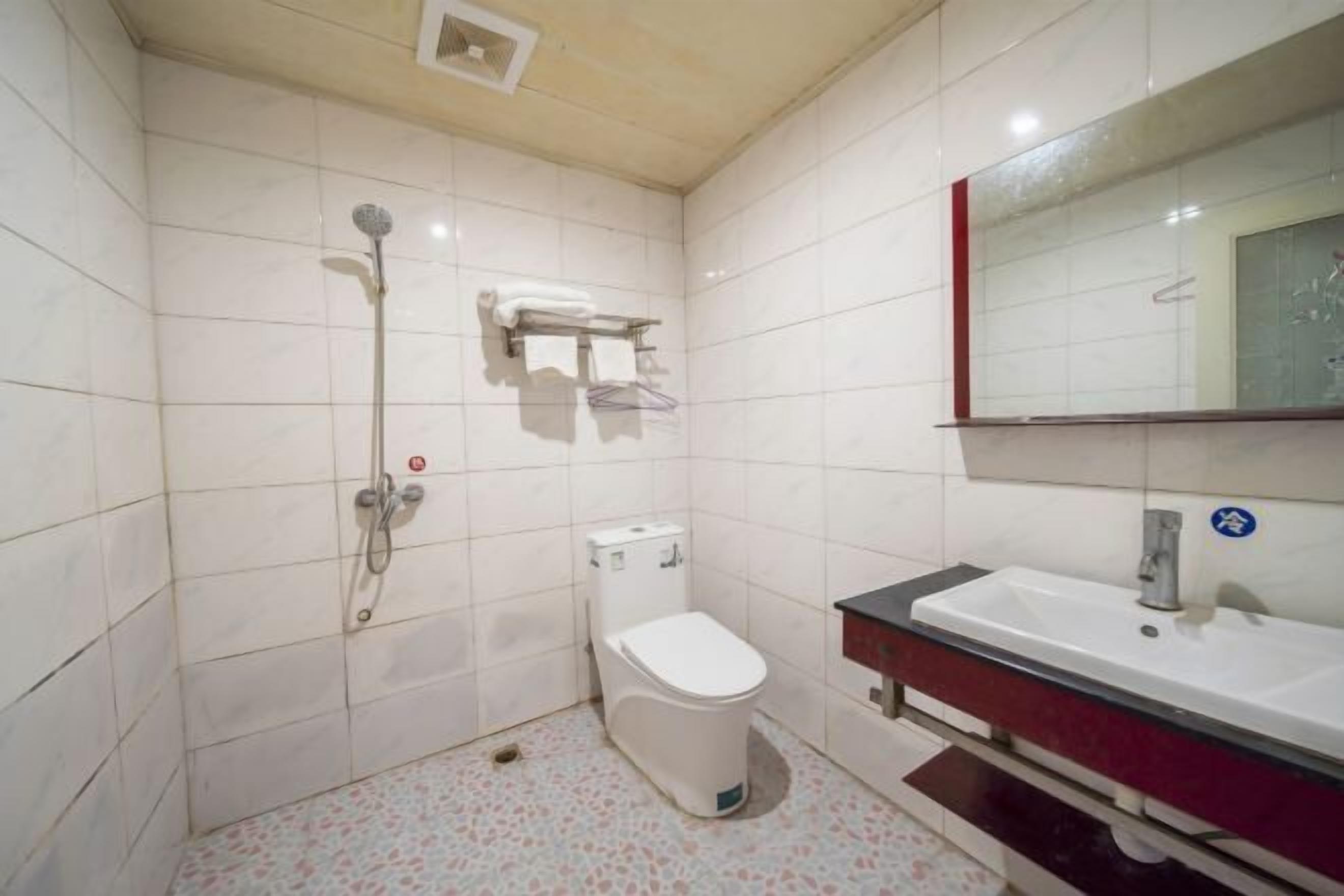 A bathroom with white tiles, a toilet, a shower, and a sink with a mirror.