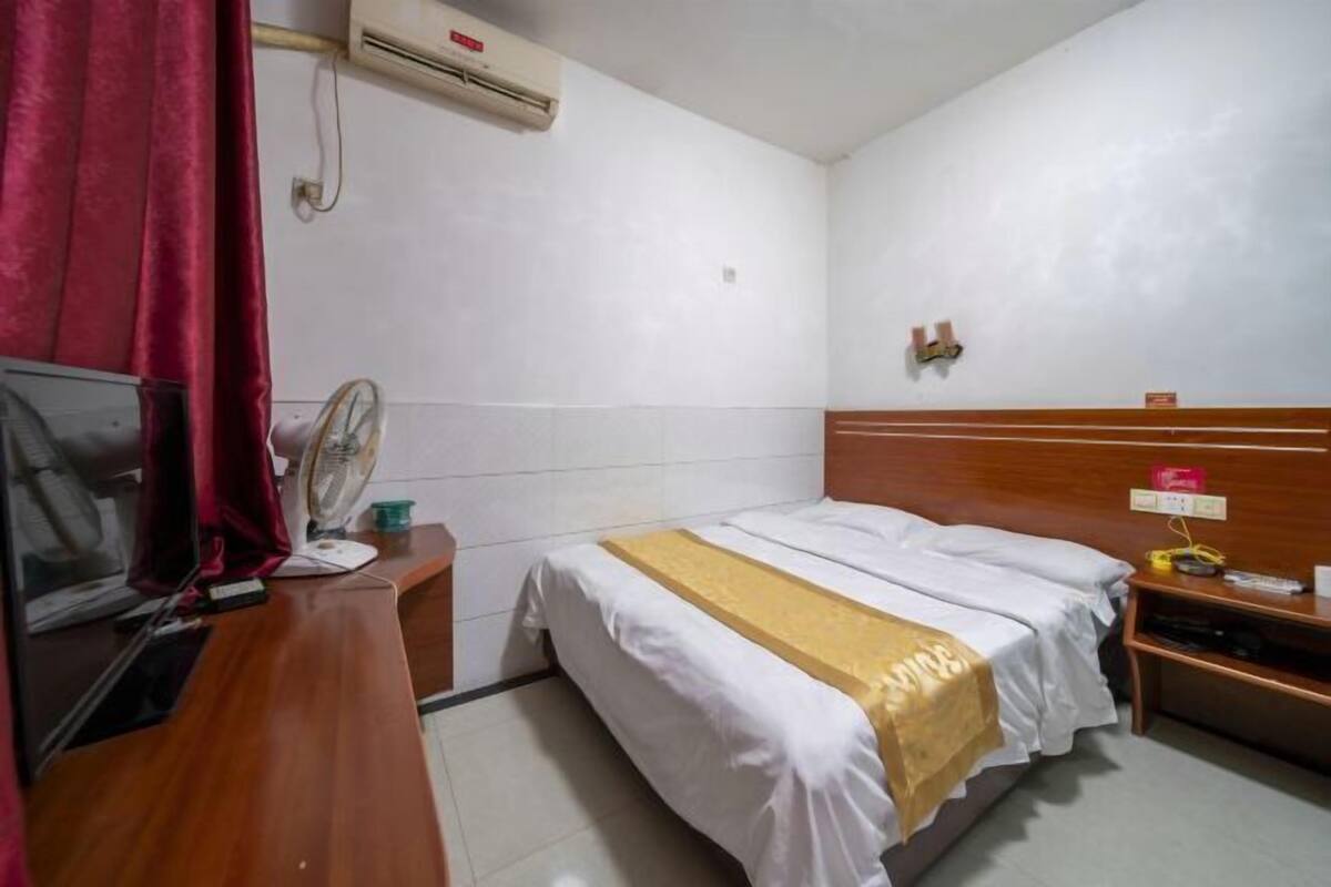 A small hotel room with a bed, a desk with a computer, a fan, and a TV.