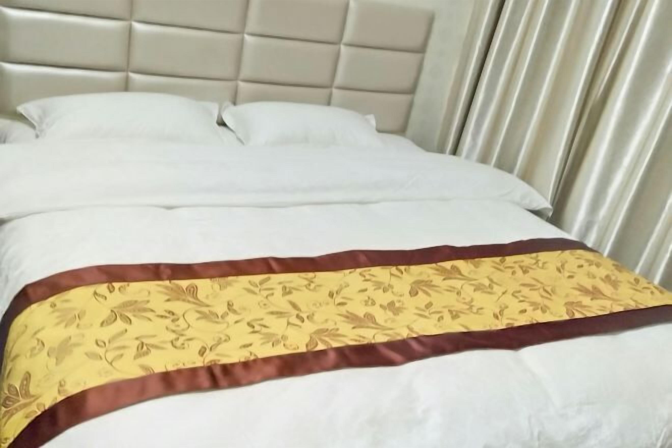 Cama com colchão branco e manta decorativa dourada e castanha.