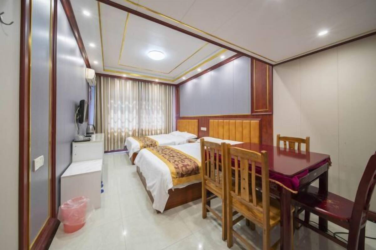 A hotel room with two beds, a wooden dining table, and a television.