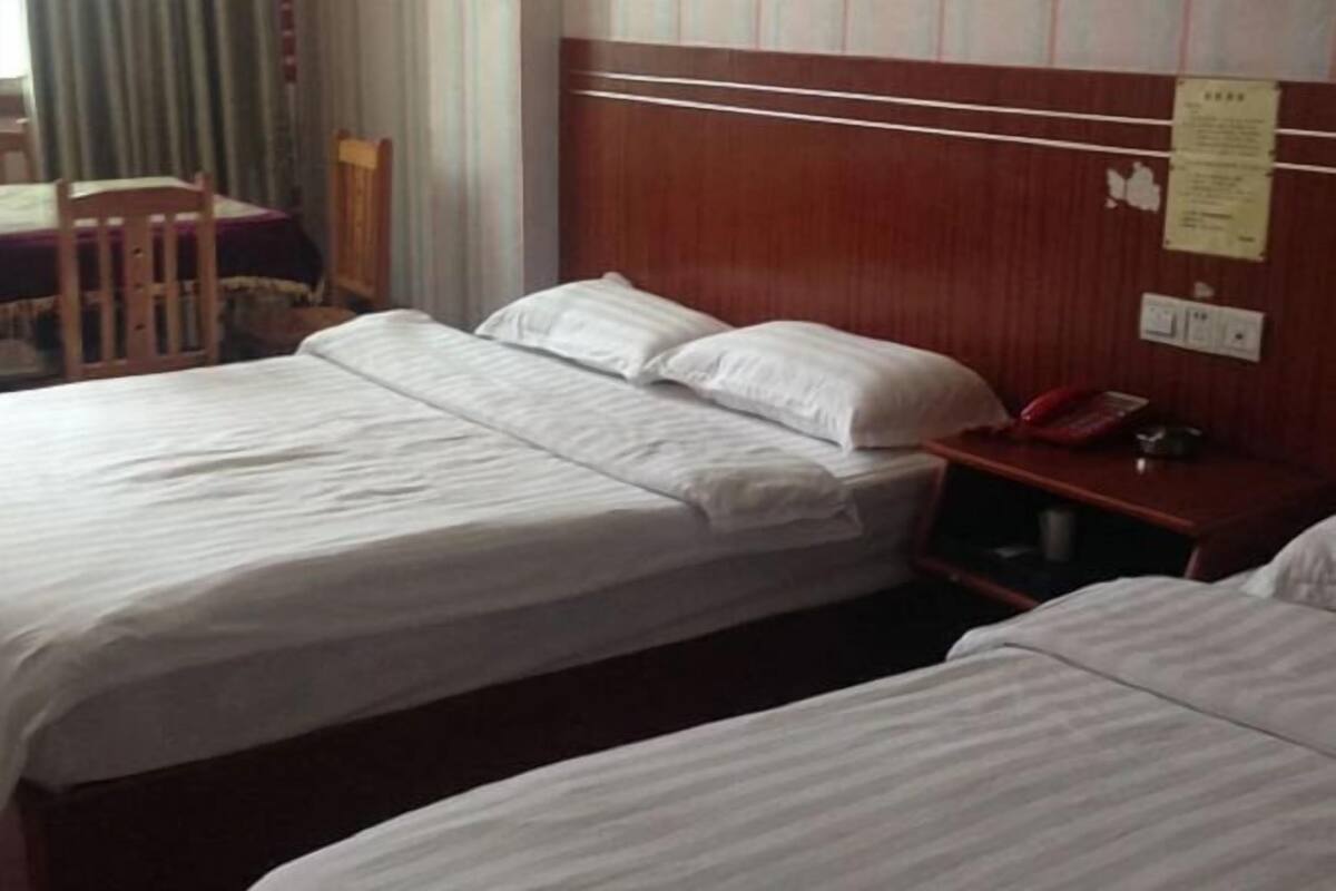 A hotel room with two beds, a wooden headboard, a bedside table with a red telephone, and a wall-mounted notice.