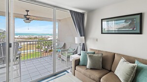 A balcony with a view of the beach, a sofa with cushions, and a framed picture on the wall. - Sunny 2BR Gulf-View Condo with Balcony & Beach Access | Magnolia House 302 (Destin)