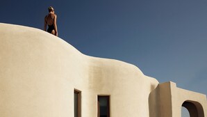 A person standing on a curved building with a clear sky. - Omeon Mykonos (Mykonos)