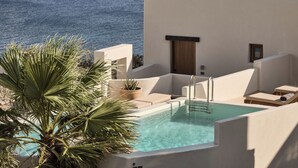 A pool area with a view of the sea, a palm tree, and a building with a door and number 203. - Omeon Mykonos (Mykonos)