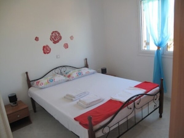 A bedroom with a bed, a nightstand, a window with a blue curtain, and wall decorations.