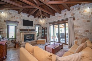 A stone-walled living room with a fireplace, wooden beams, a sofa, and a television.