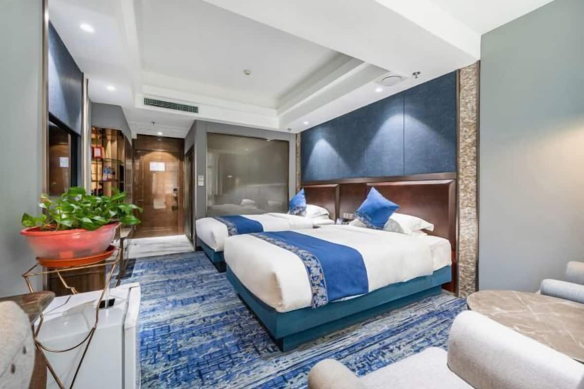 A hotel room with two beds, a large potted plant, a desk, and a seating area.