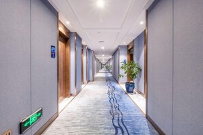 A hotel corridor with doors on both sides, a carpeted floor, and a potted plant on the right. - Ann Keats Hotel (Lanzhou)