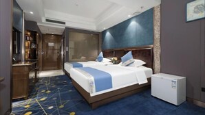 Een hotelkamer met een groot bed, een kleine koelkast, een bureau en een badkamer.
