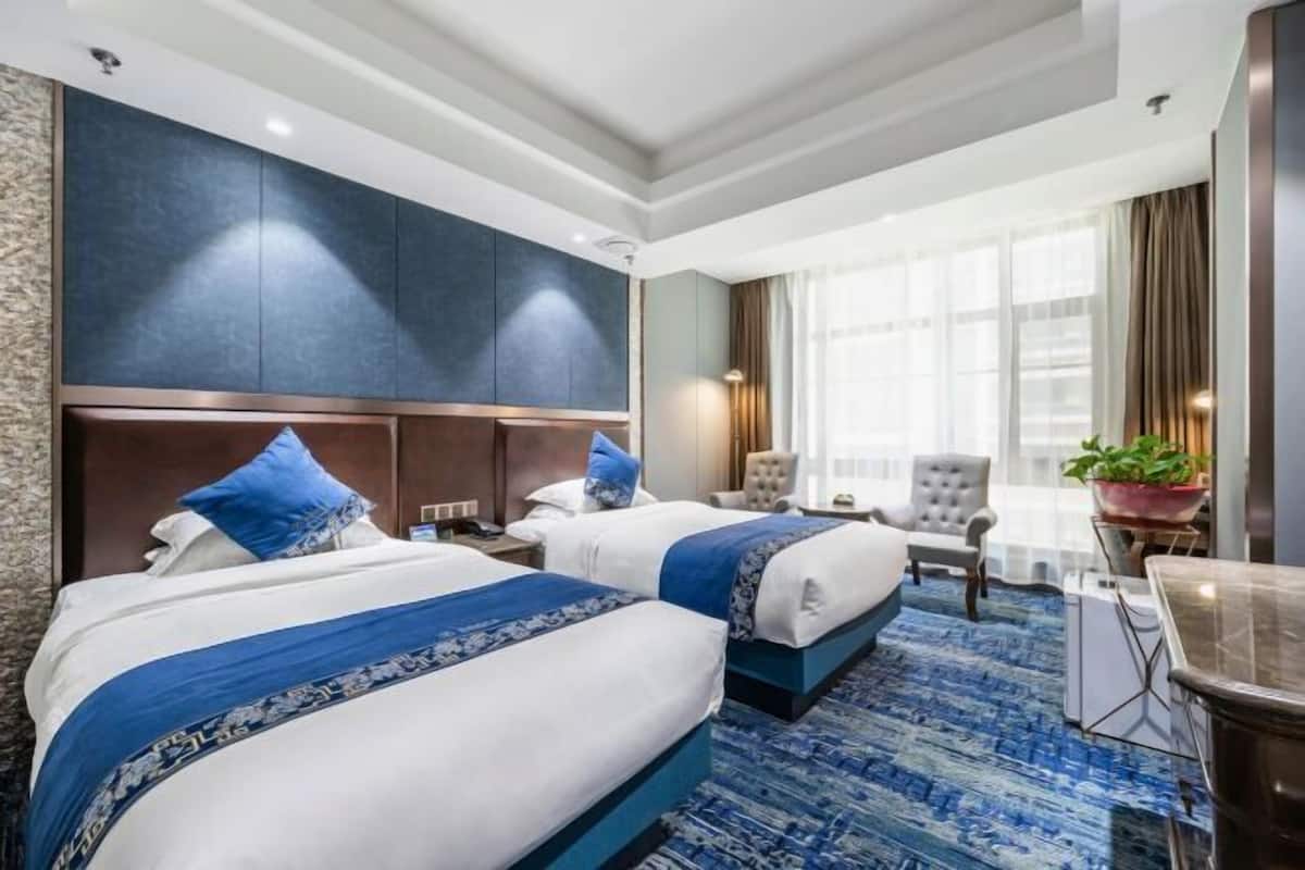 A hotel room with two beds, a large window with curtains, a desk, and a chair.