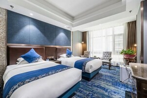 A hotel room with two beds, a large window with curtains, a desk, and a chair.