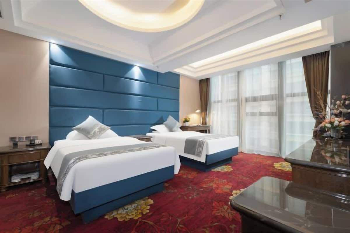 A hotel room with two beds, a desk, a nightstand, a TV, and a large window with curtains.